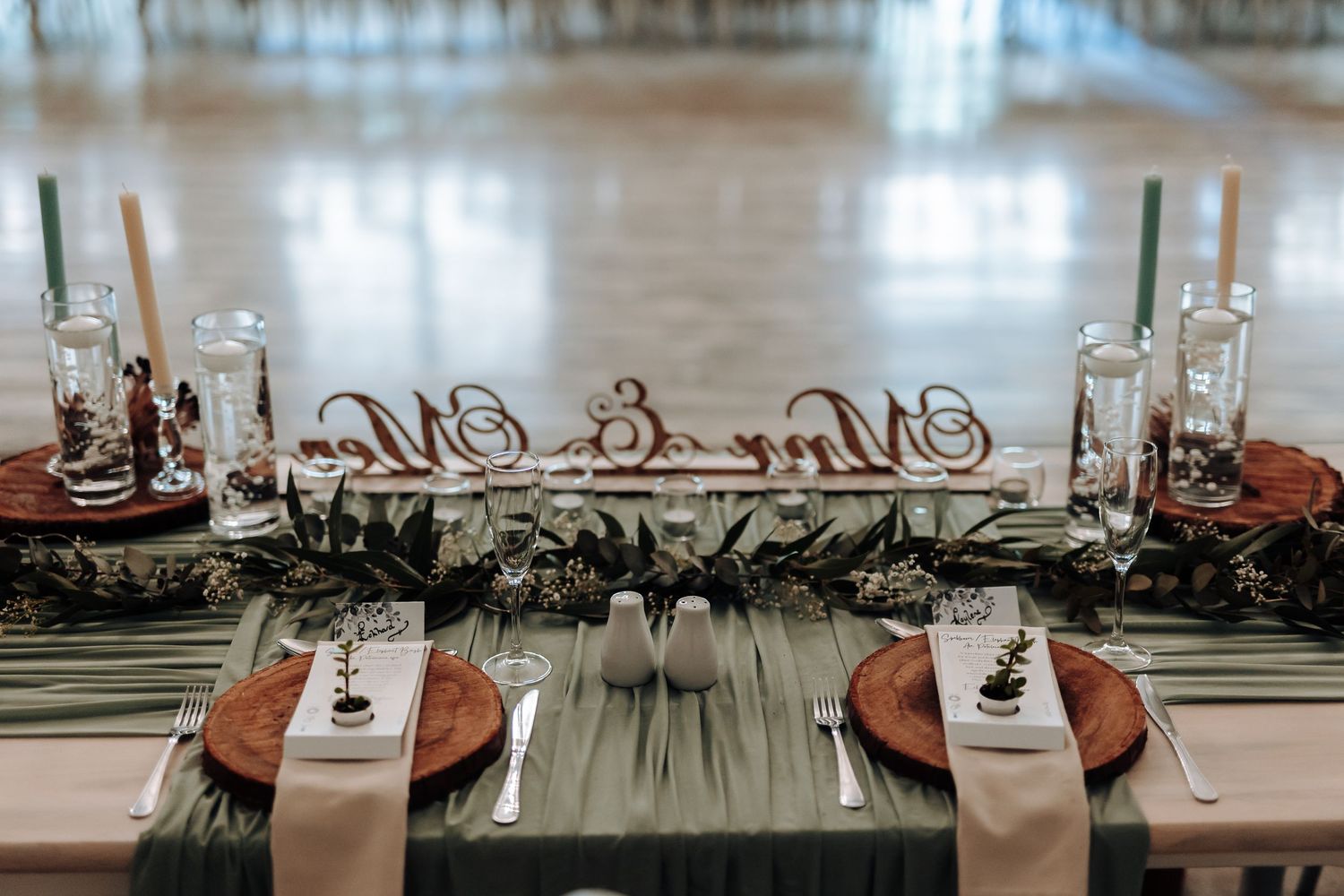 Modern table setting with candles, greenery and metallic accents for a wedding reception.