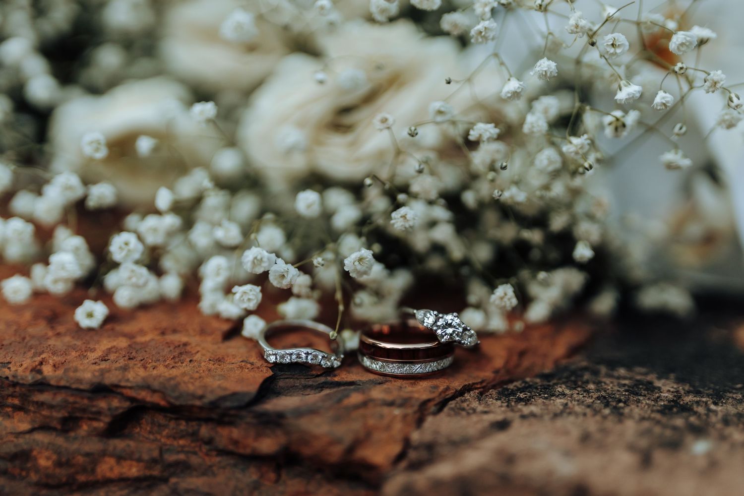 Wedding rings displayed with delicate baby's breath flowers on wooden surface.