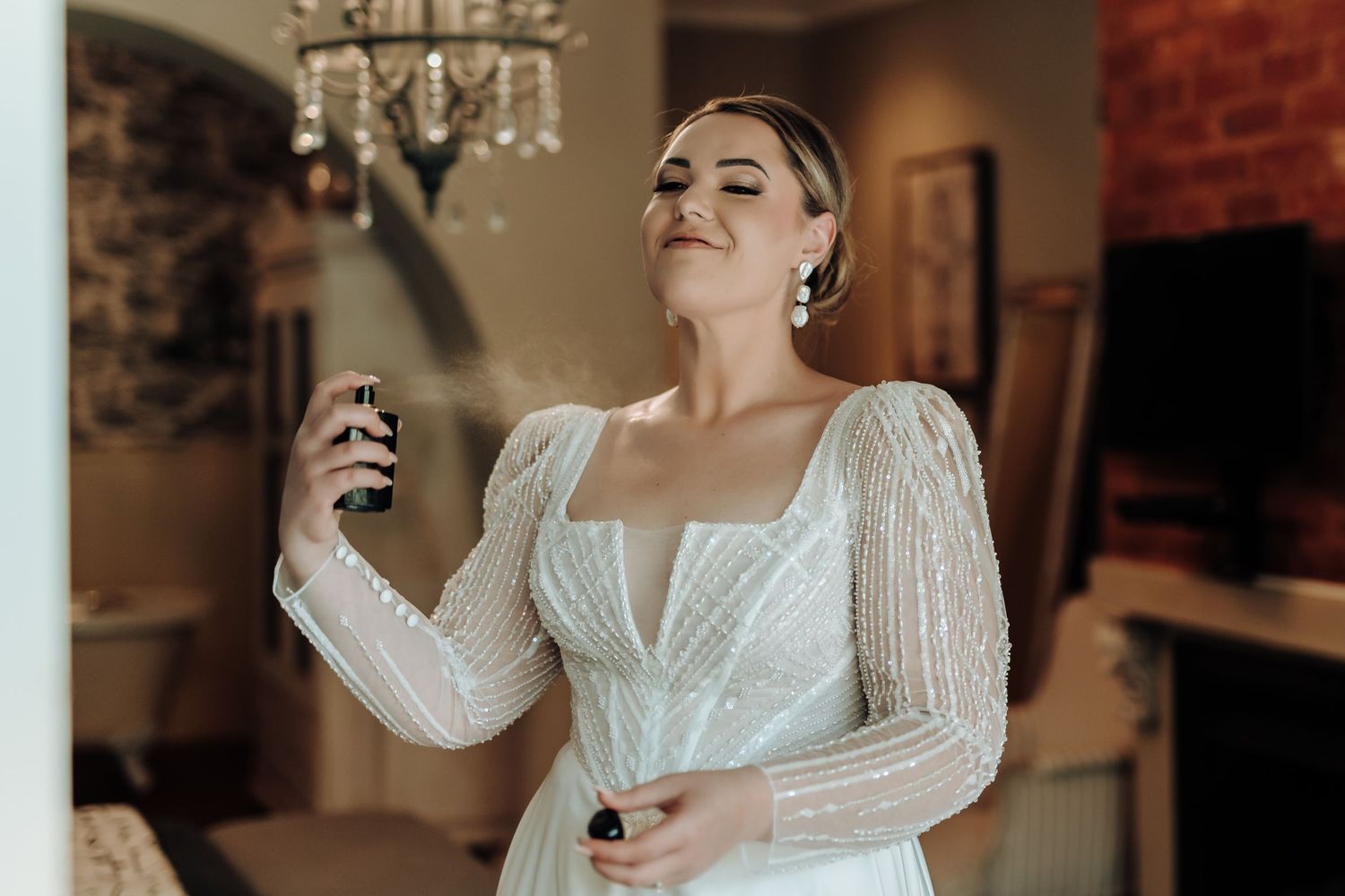 Ethereal wedding dress with beaded mesh sleeves and square neckline in soft indoor lighting.