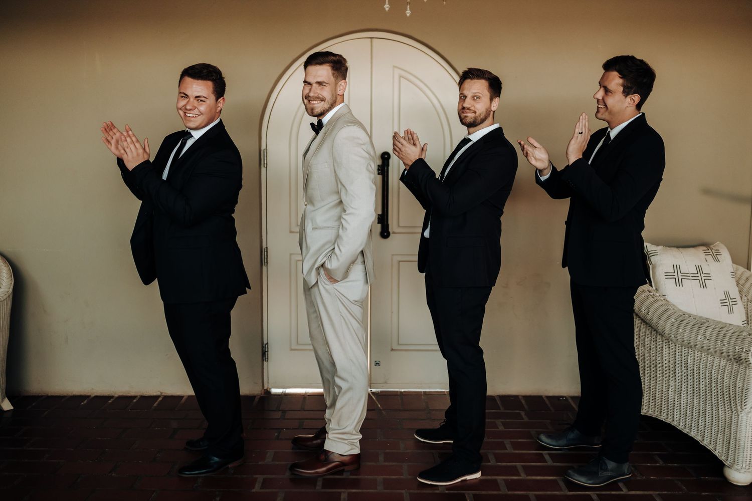 Groomsmen perform choreographed dance pose while groom stands center in light colored suit.