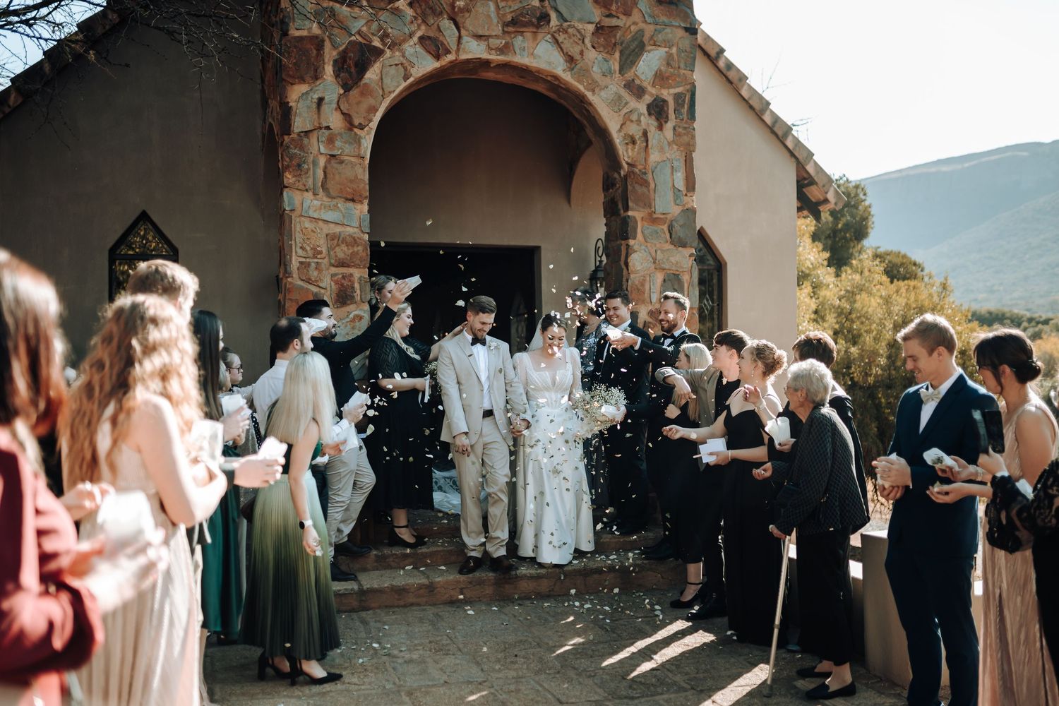 Guests line pathway outside stone chapel entrance during wedding celebration.
