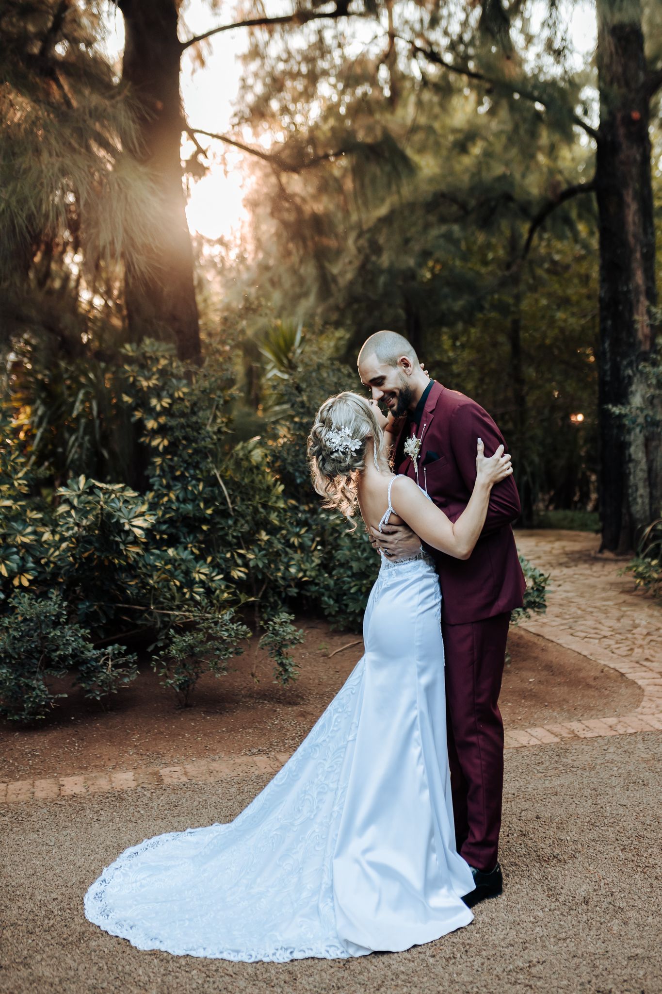 A romantic wedding portrait of a couple embracing on a garden path at sunset.