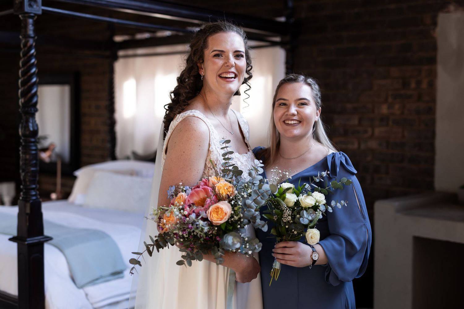 Wedding party members share a joyful moment while holding beautiful floral bouquets in a rustic indoor setting.