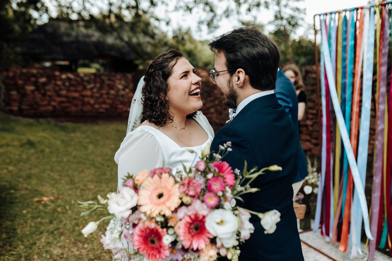 A joyful moment between newlyweds with a vibrant bouquet of pink and white flowers.