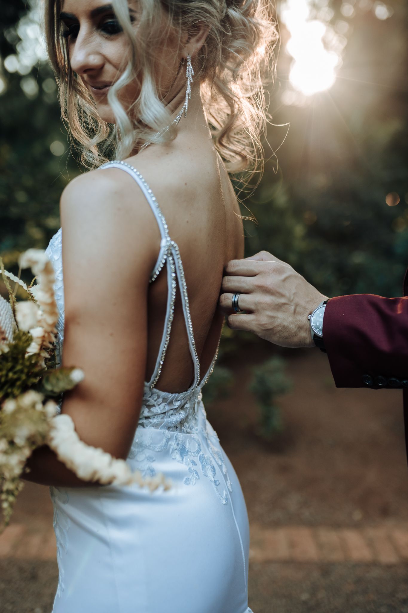 Detail shot of an elegant white wedding dress with beaded straps in golden sunlight.