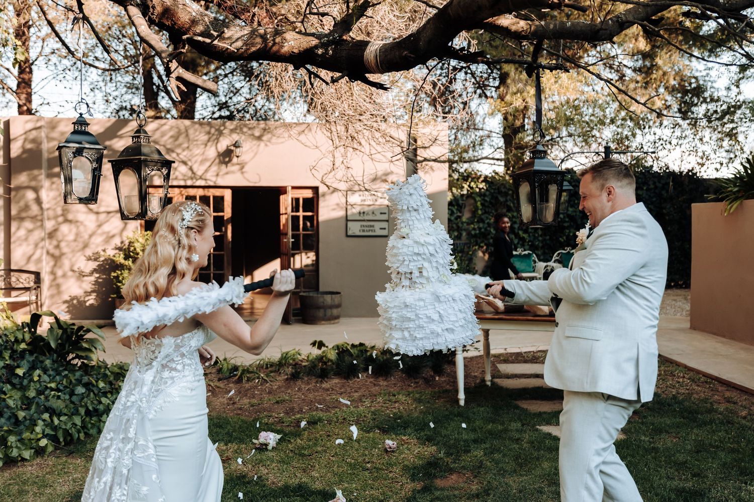 A couple playfully enjoys their wedding cake cutting moment in an outdoor garden setting.