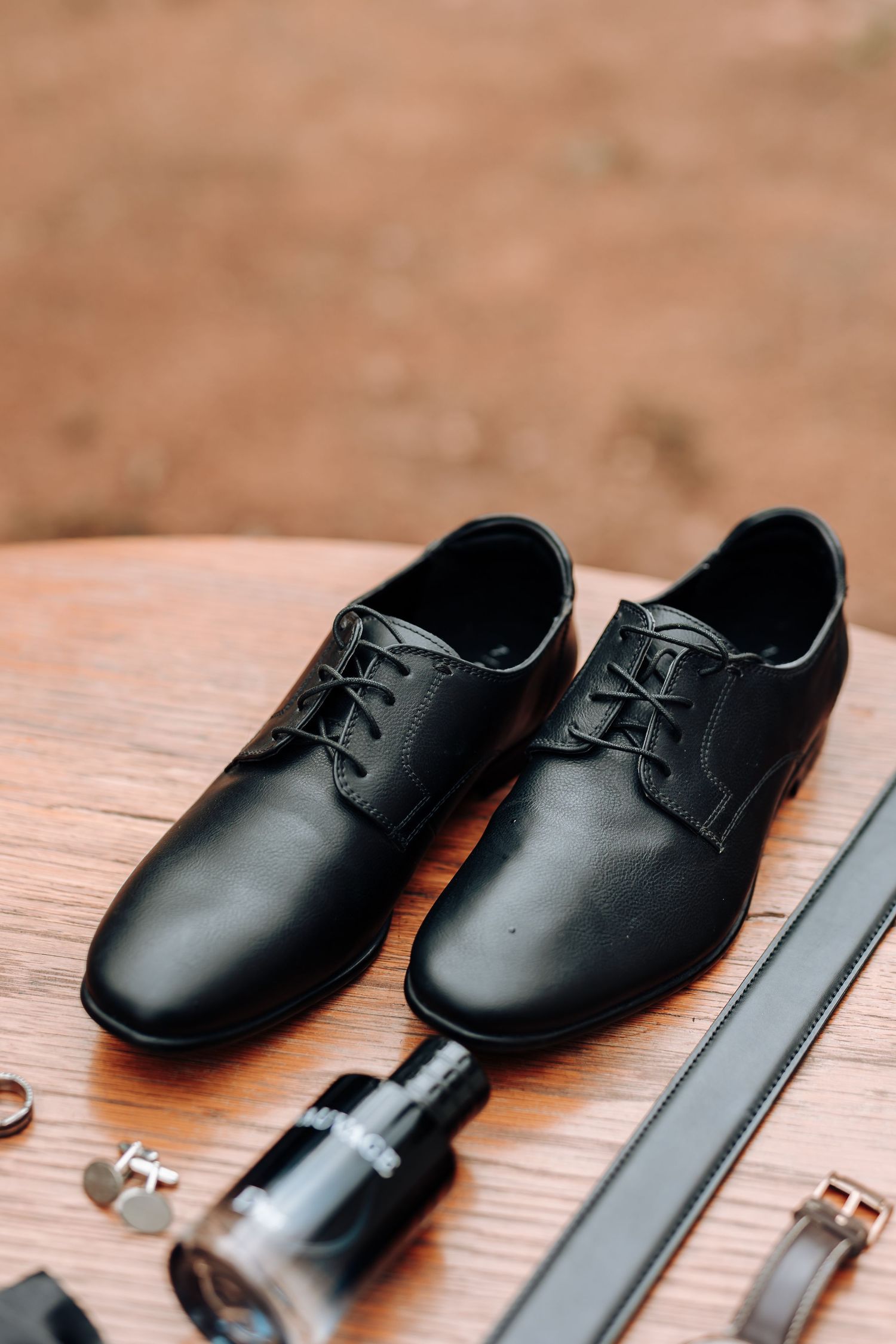 Classic black leather dress shoes with accessories on wooden surface.