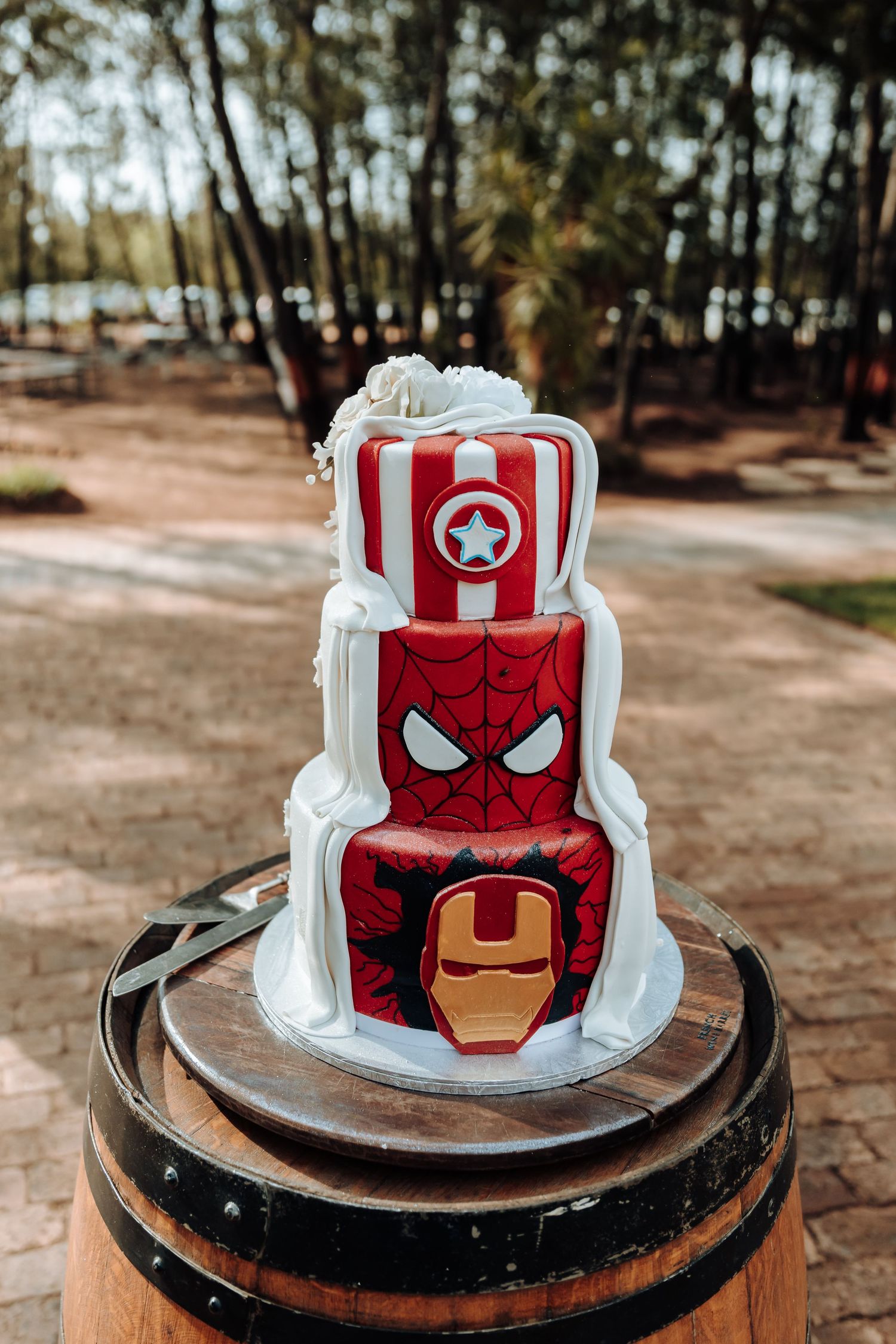 Marvel-themed wedding cake featuring Captain America, Spider-Man and Iron Man designs on wooden barrel.