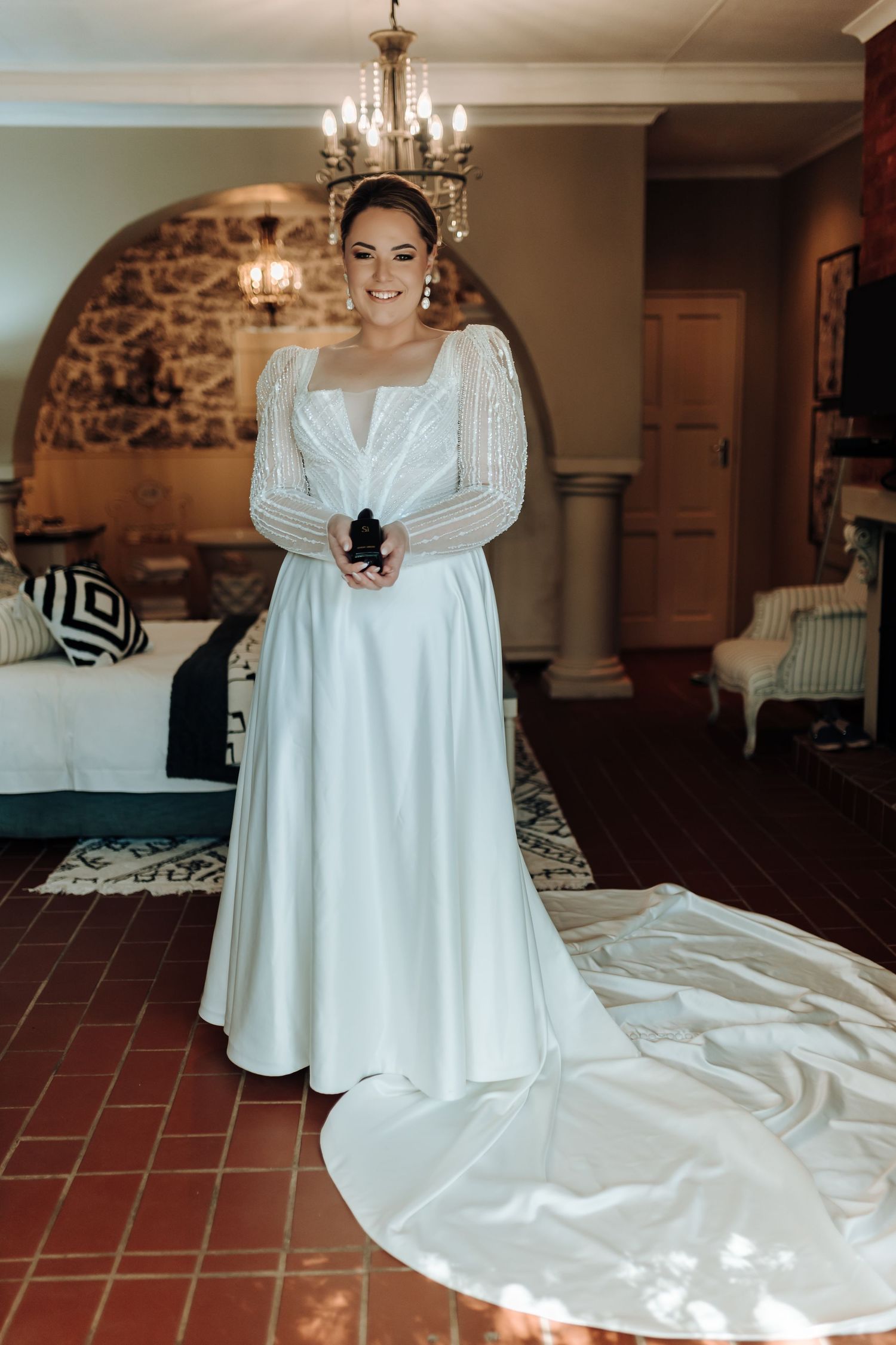 Full-length wedding dress photo showing dramatic train and beaded sleeves in rustic venue.