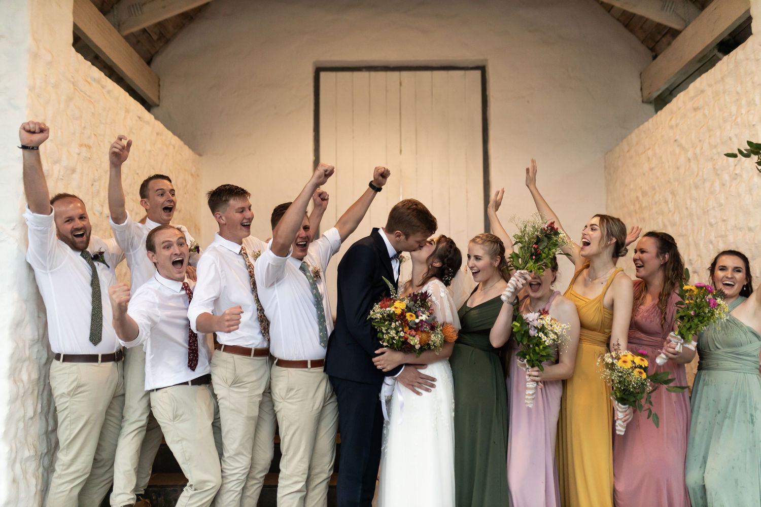 Celebratory wedding party photo with groomsmen in white shirts raising arms in excitement.
