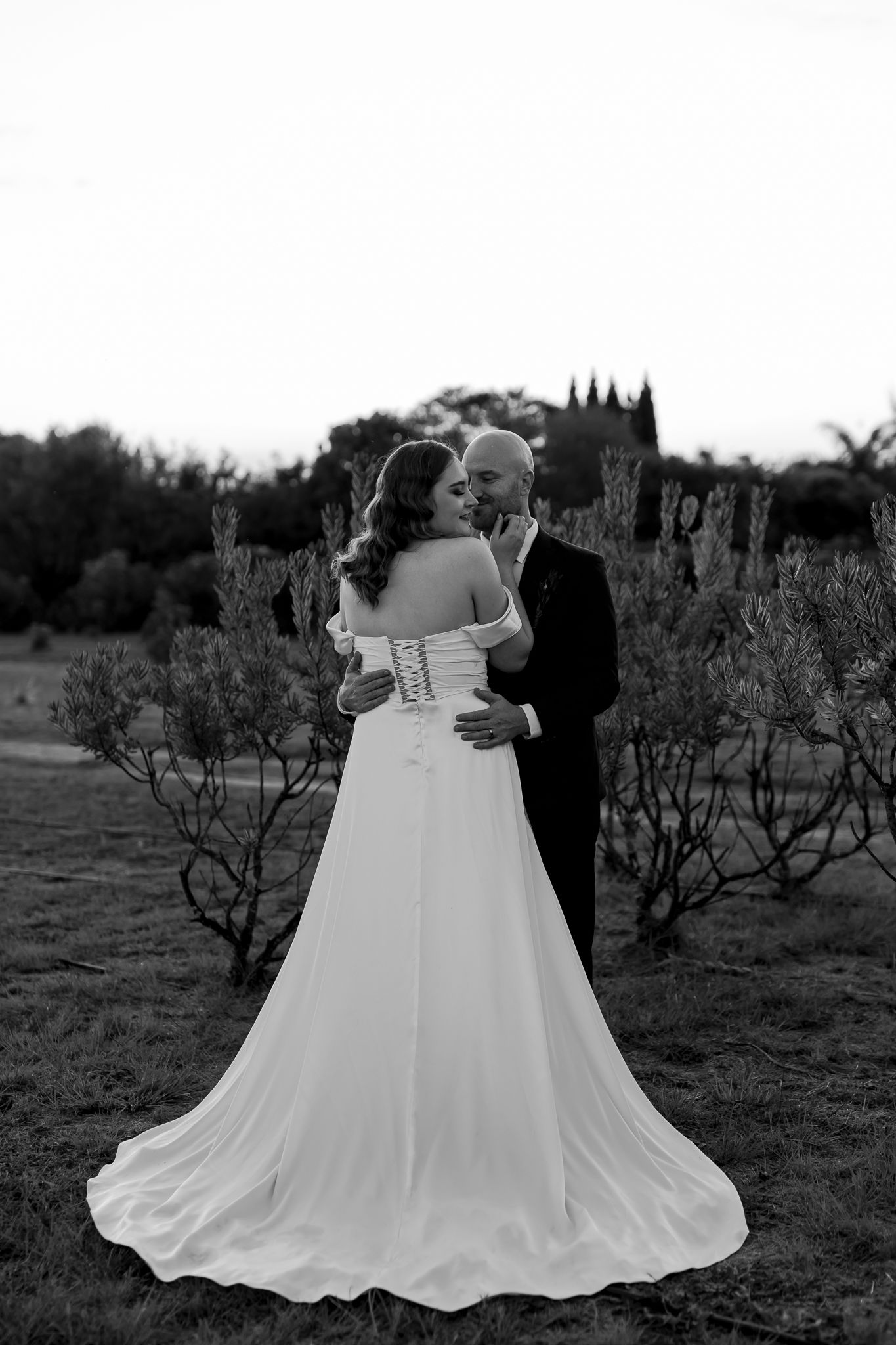 Black and white photo showing the back of a bride's dress as couple embraces.