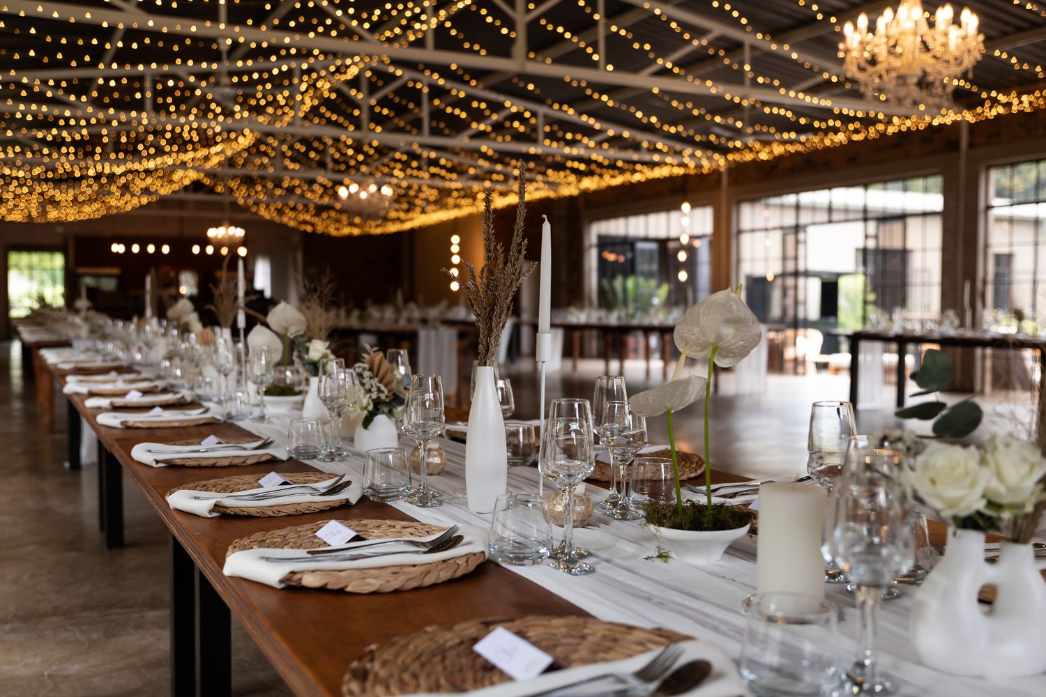 Wedding reception venue with string lights overhead and long tables set with elegant place settings.