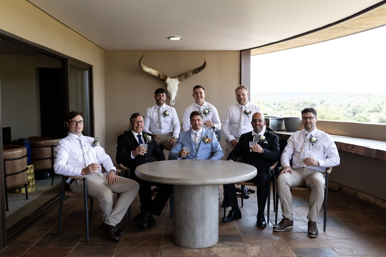 Wedding party relaxing around circular table with longhorn decor on wall.