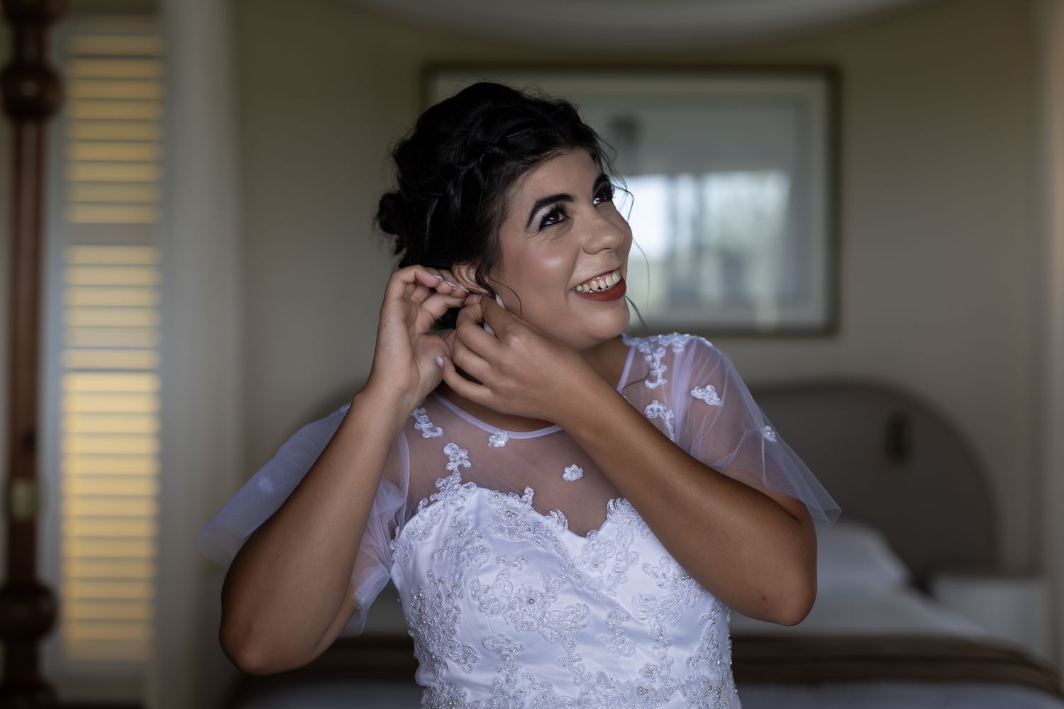 A person in a lace wedding gown touches their earrings while getting ready.