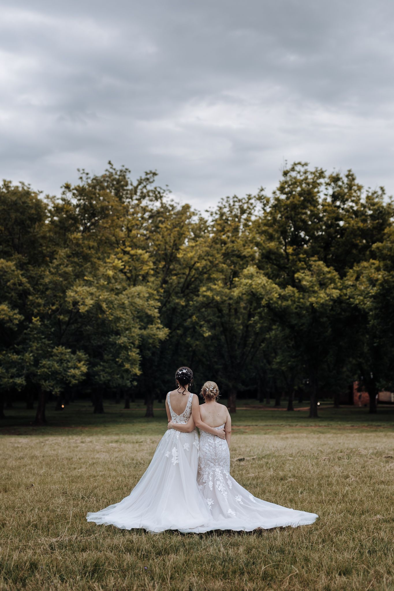 Two people in white lace wedding dresses sharing an intimate moment in a garden setting.