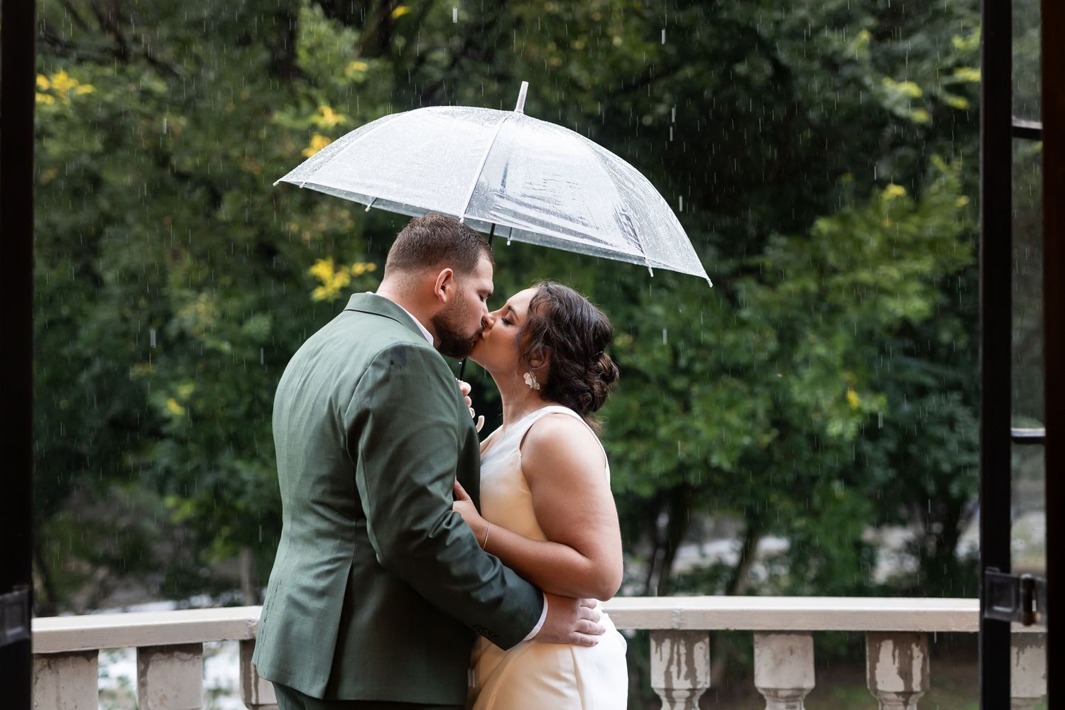 Couple shares romantic moment under clear umbrella during light rain.