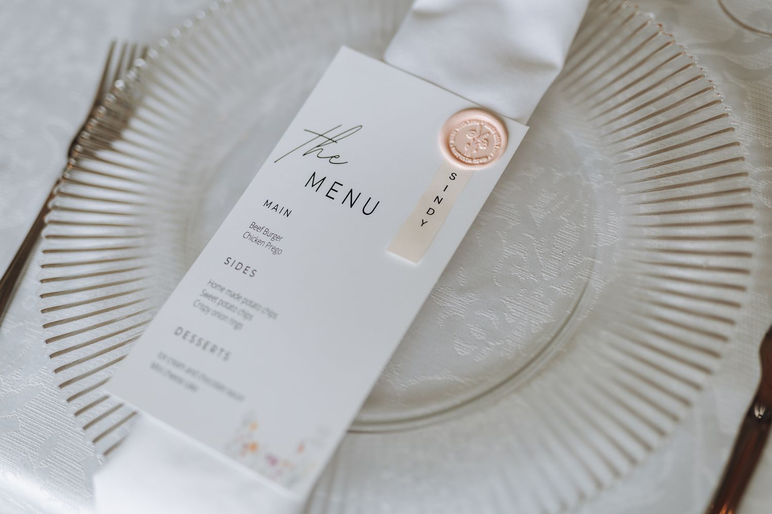 Minimalist wedding menu card with wax seal placed on a textured glass plate.