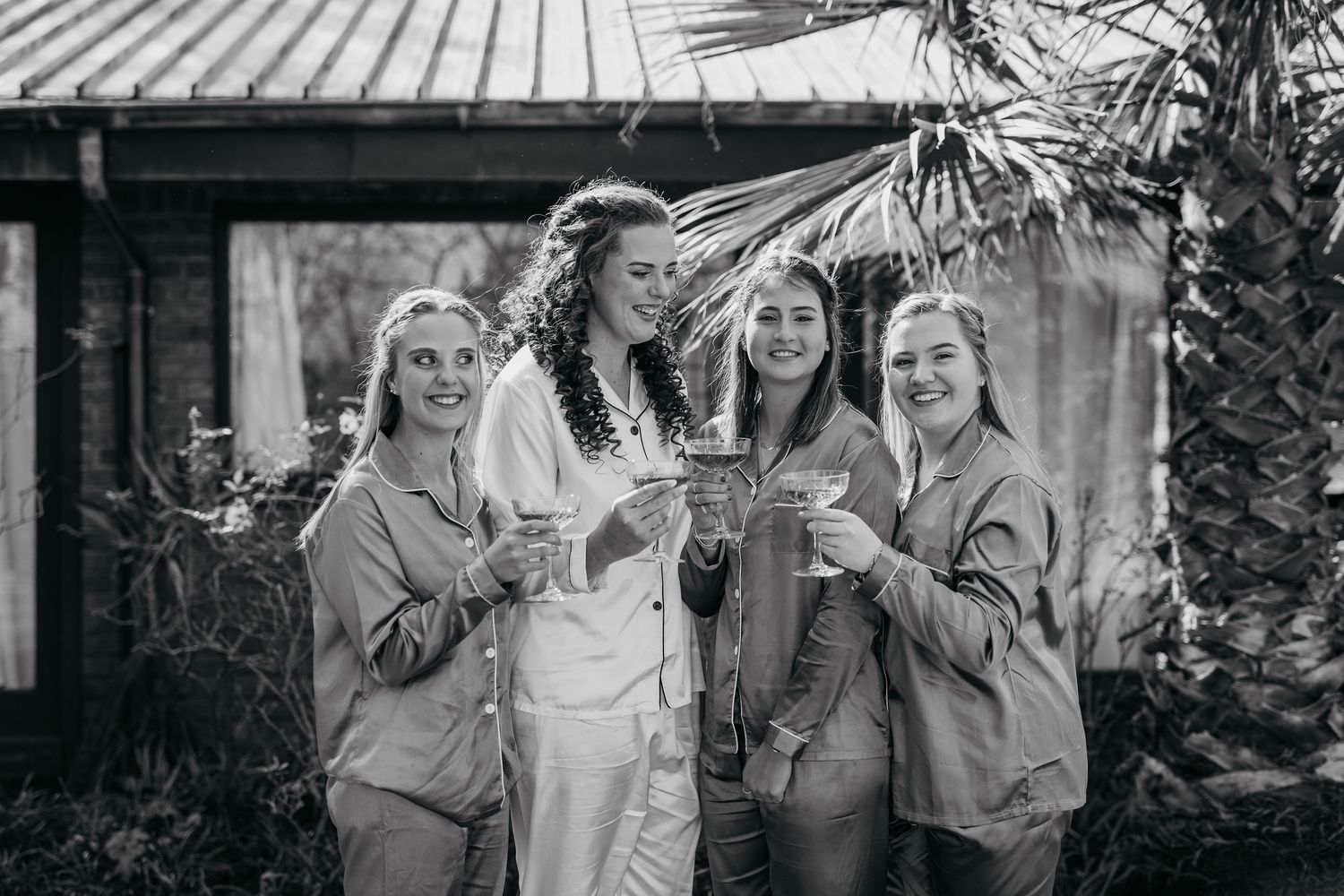 Black and white photo of people toasting with glasses outdoors in casual attire.