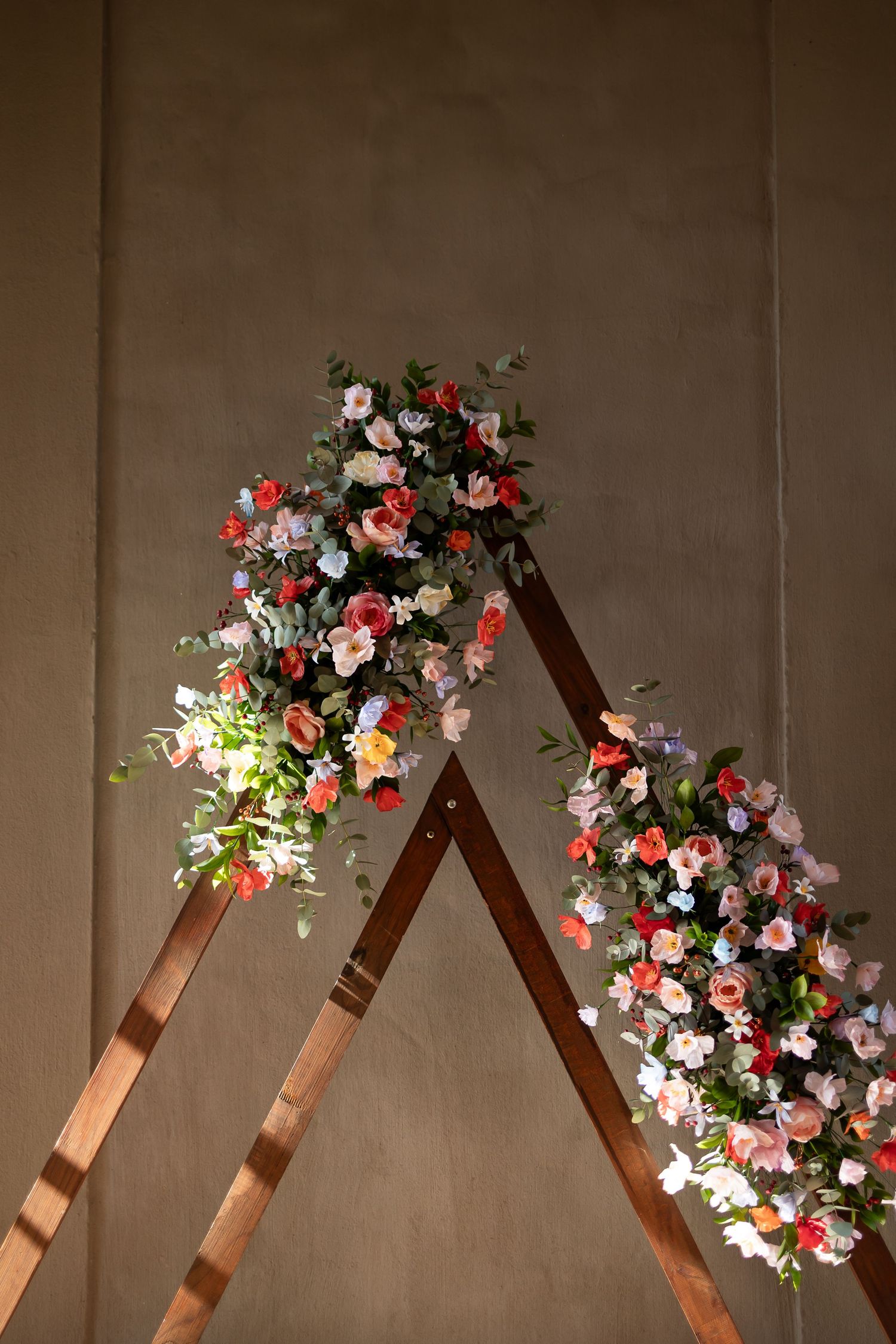 A wooden A-frame arch decorated with pink and white roses and greenery against a neutral wall.
