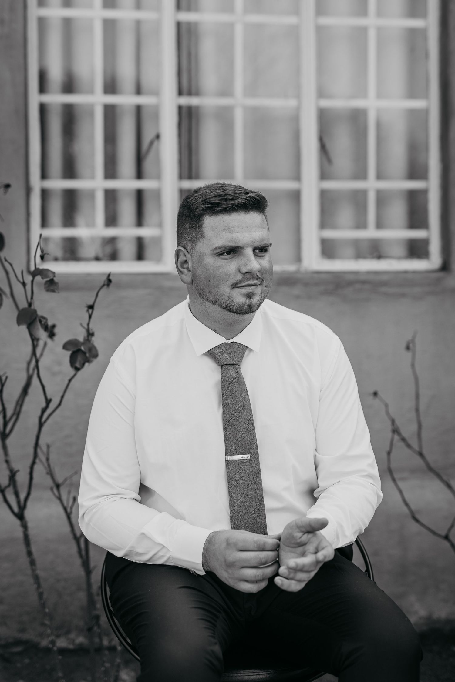 Black and white photos of person wearing white dress shirt and tie sitting outdoors.