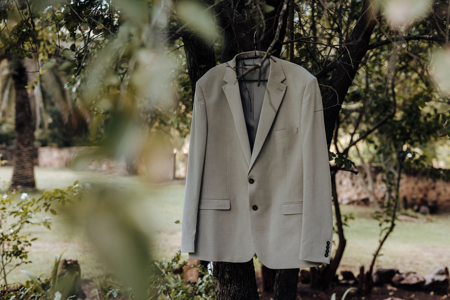 Light grey suit jacket hanging outdoors against natural foliage background.