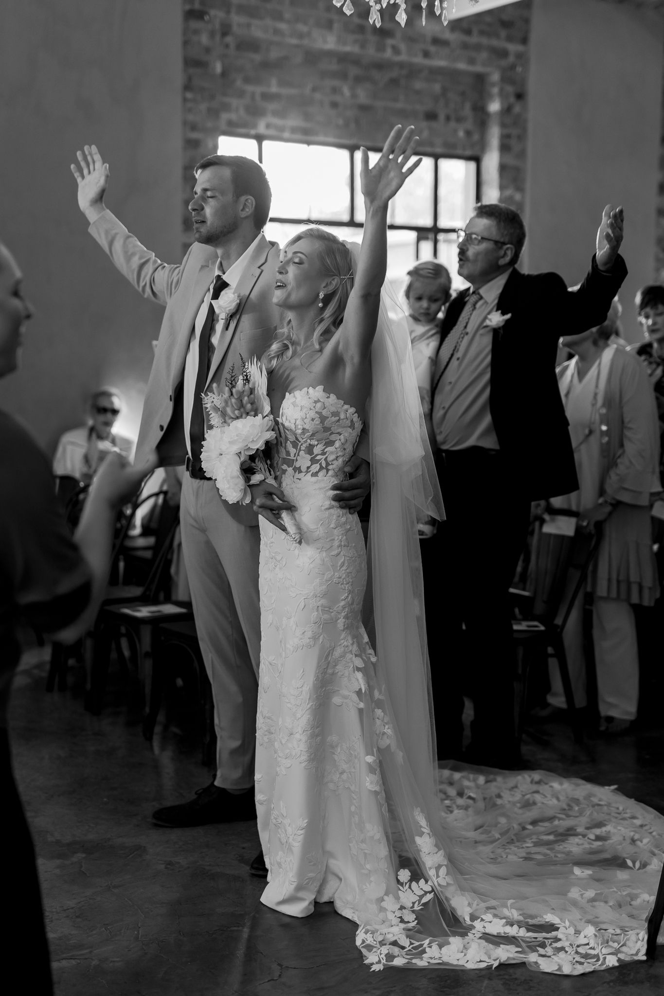 Wedding celebration with guests raising hands in joy at industrial-style venue.