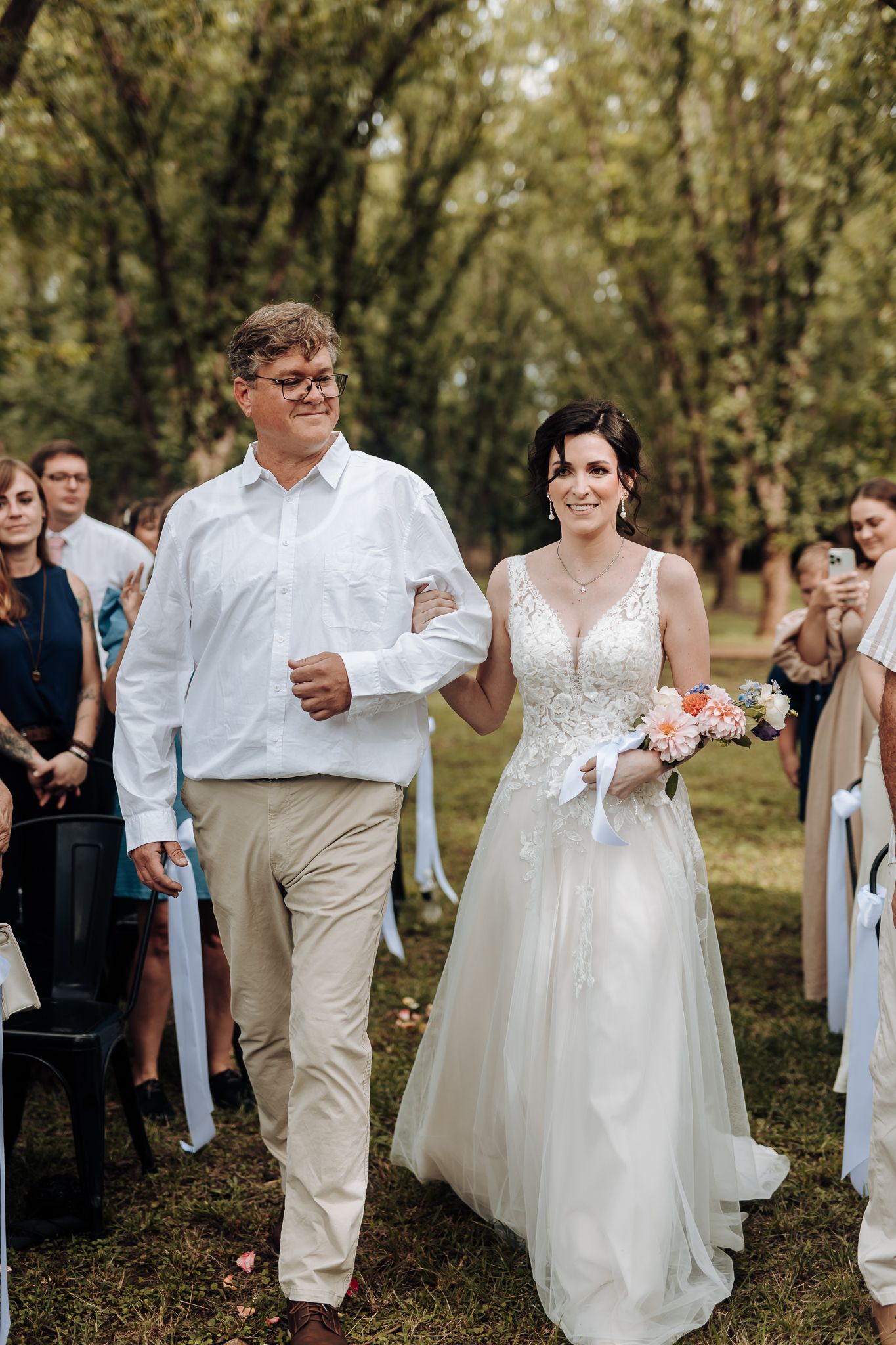 Two people walk arm in arm down aisle during outdoor wedding ceremony.