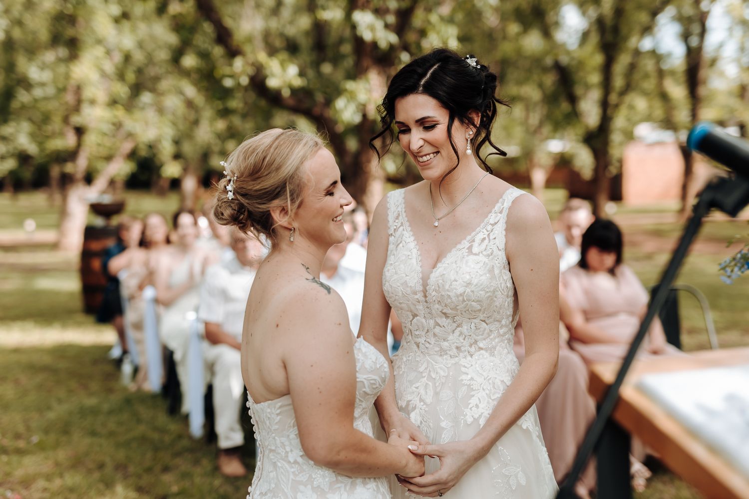 Intimate wedding ceremony moment in sunny garden with guests seated in background.