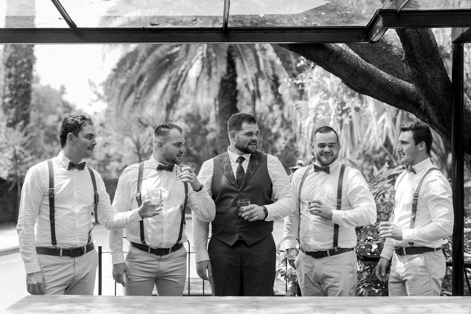 Black and white photo of groomsmen laughing together at an outdoor reception.