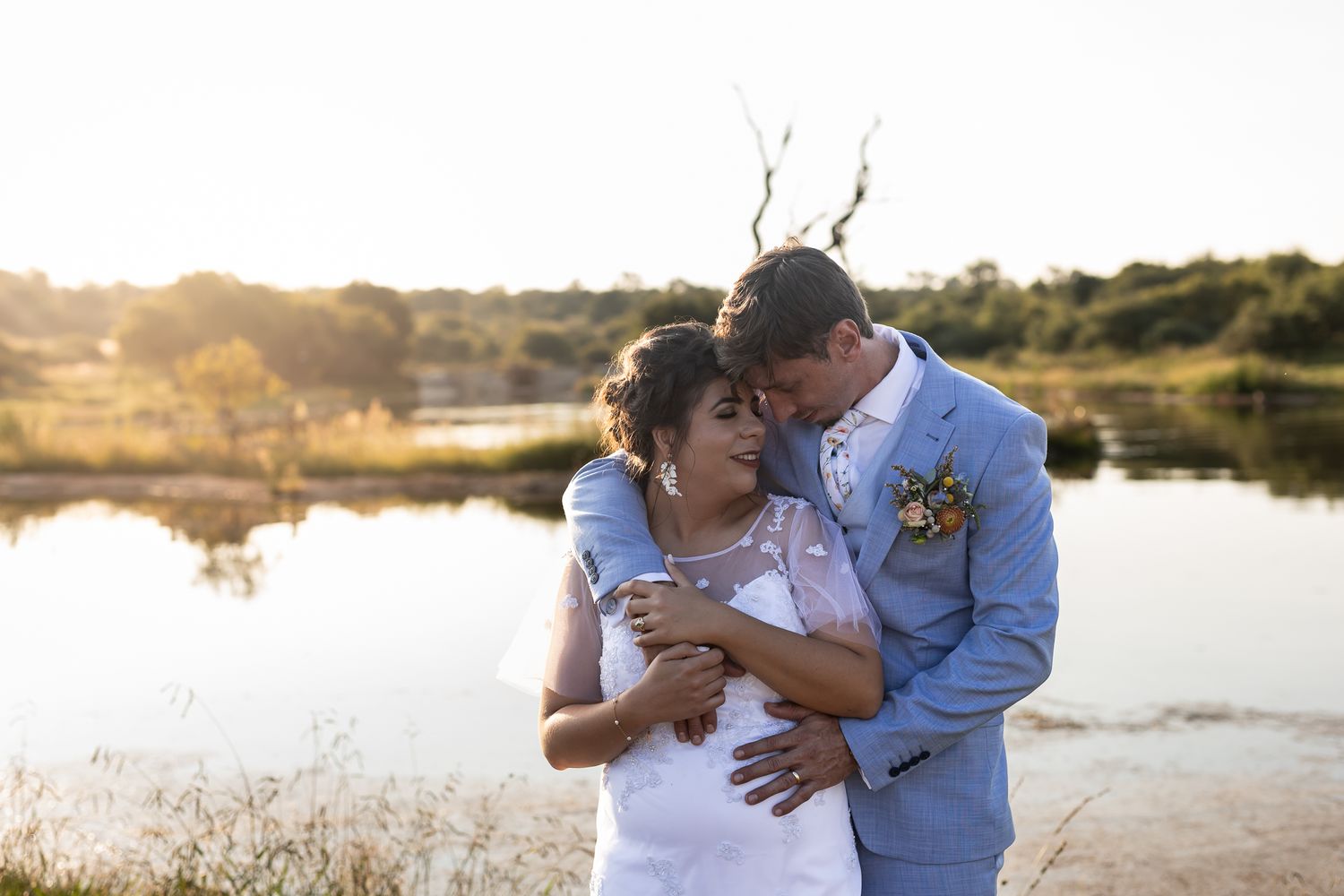 A couple embraces tenderly near a tranquil lake during golden hour.