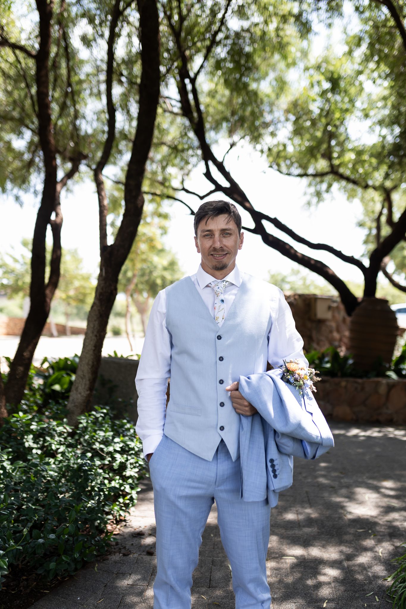 Formal attire featuring light blue vest and white shirt in outdoor garden setting.