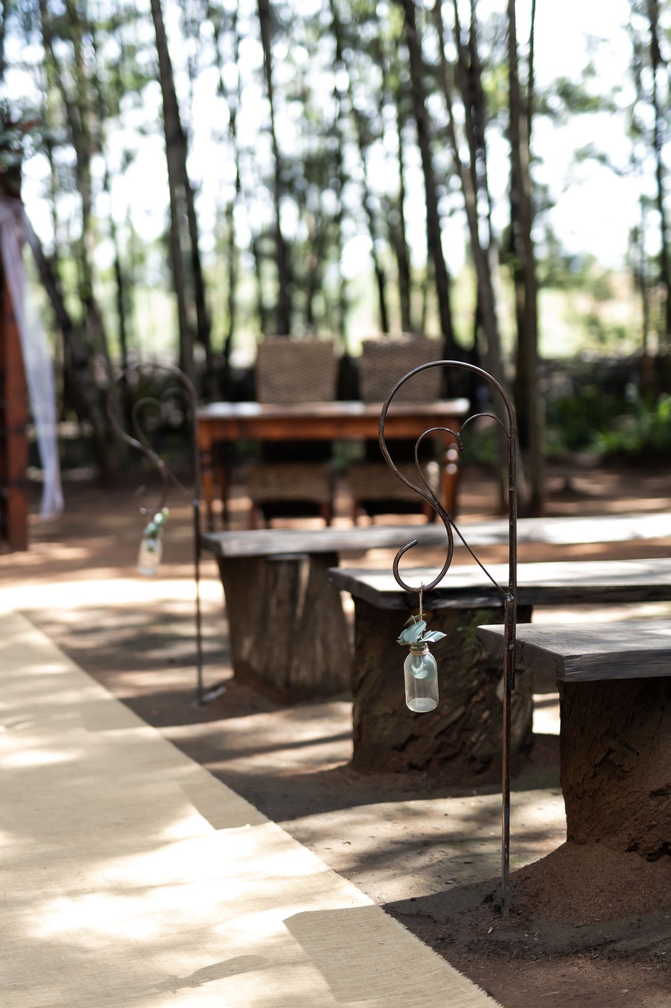 Outdoor wedding aisle with shepherd hooks holding glass jar decorations in a wooded setting.