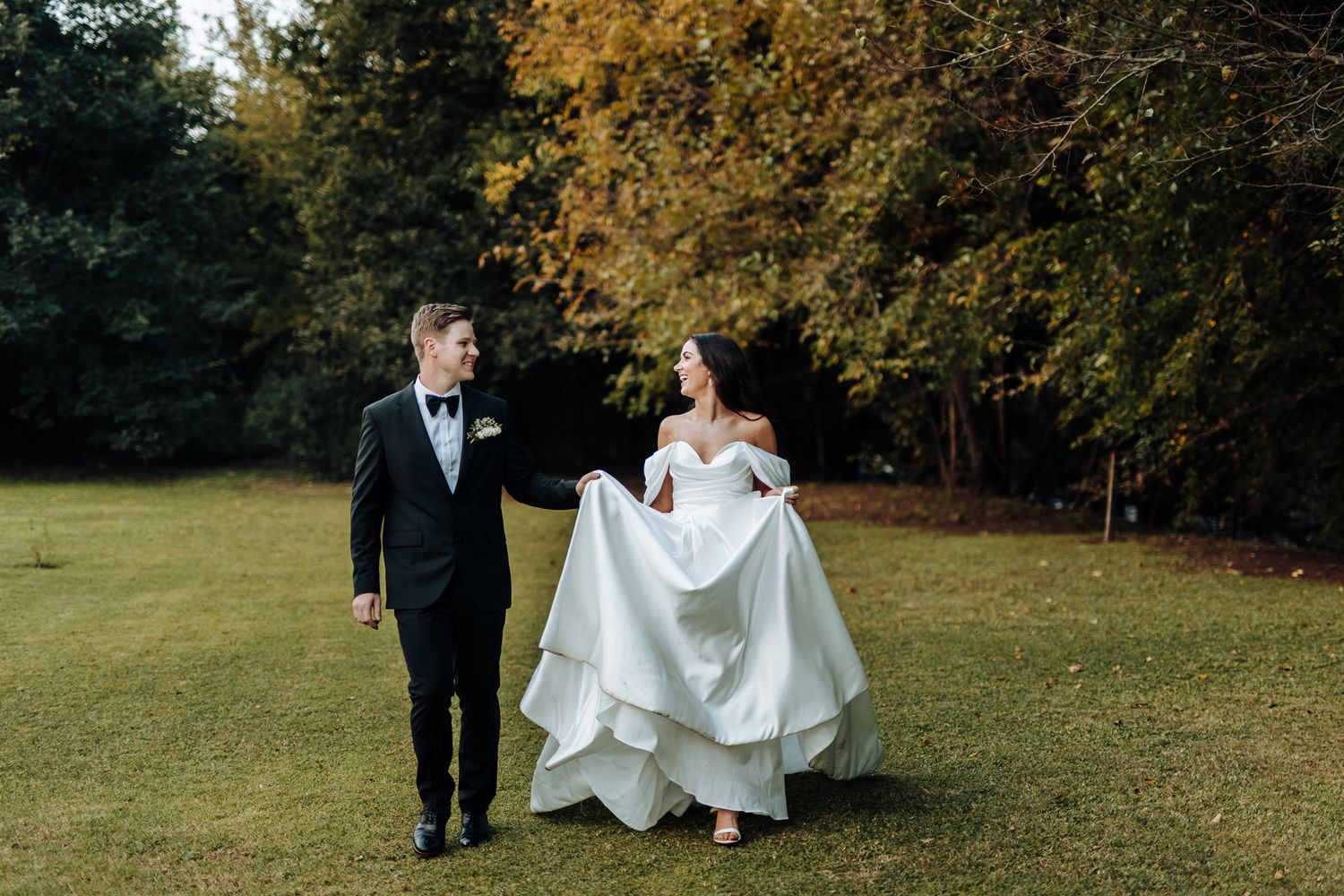 A playful wedding portrait of newlyweds walking across an autumn lawn.