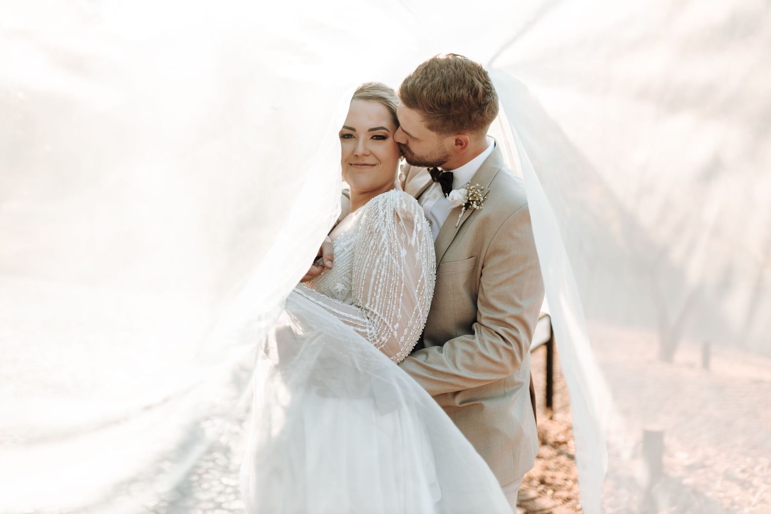 Elegant wedding couple shares tender moment with flowing veil in natural light.