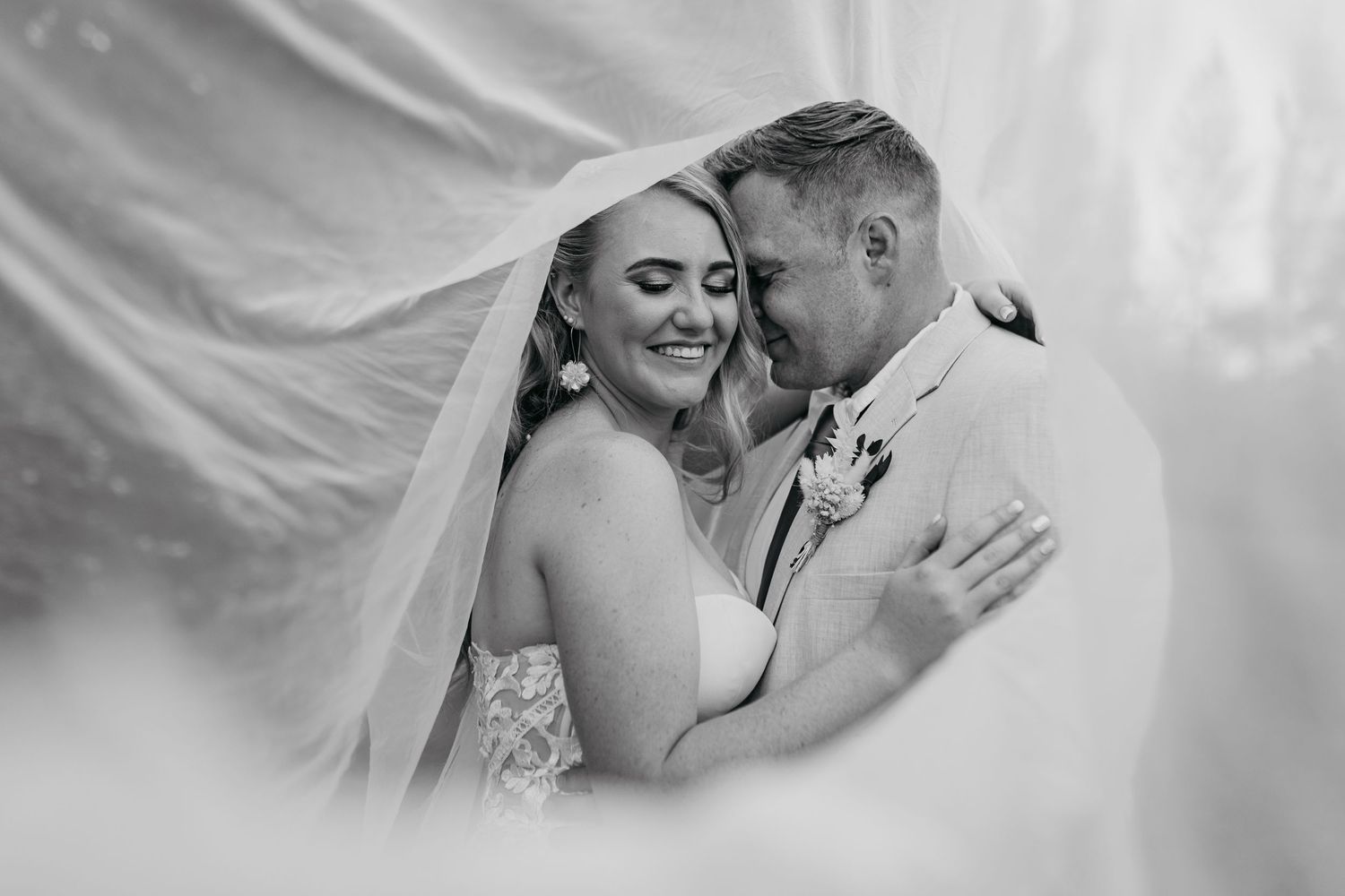 Romantic black and white portrait of newlyweds sharing intimate moment under veil.