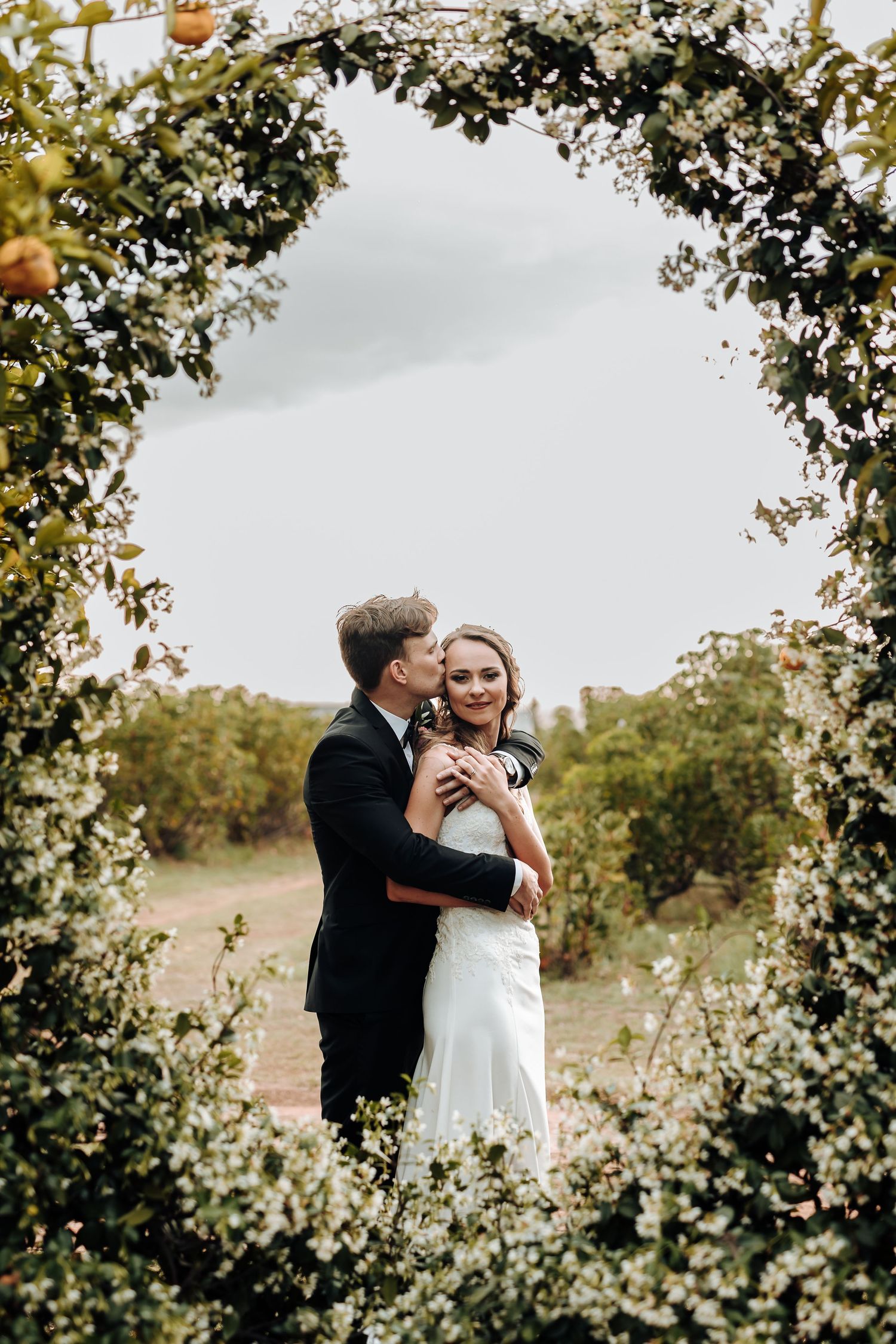 Wedding couple shares intimate moment under floral arch during outdoor ceremony.