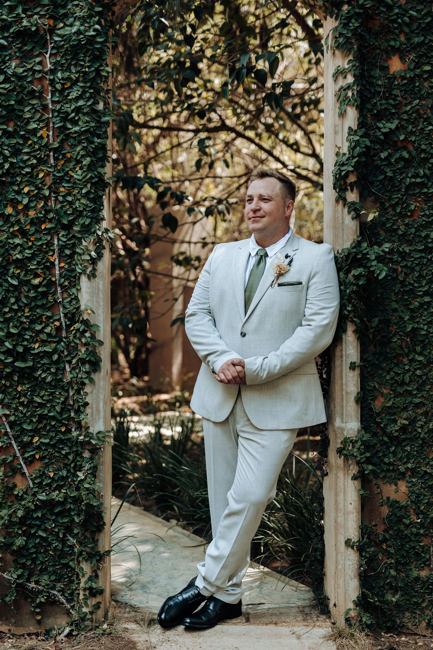 Wedding portrait of person in light suit standing in ivy-covered doorway.