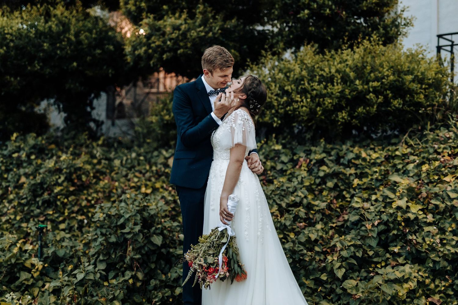 Intimate wedding moment captured against a backdrop of green foliage and natural scenery.