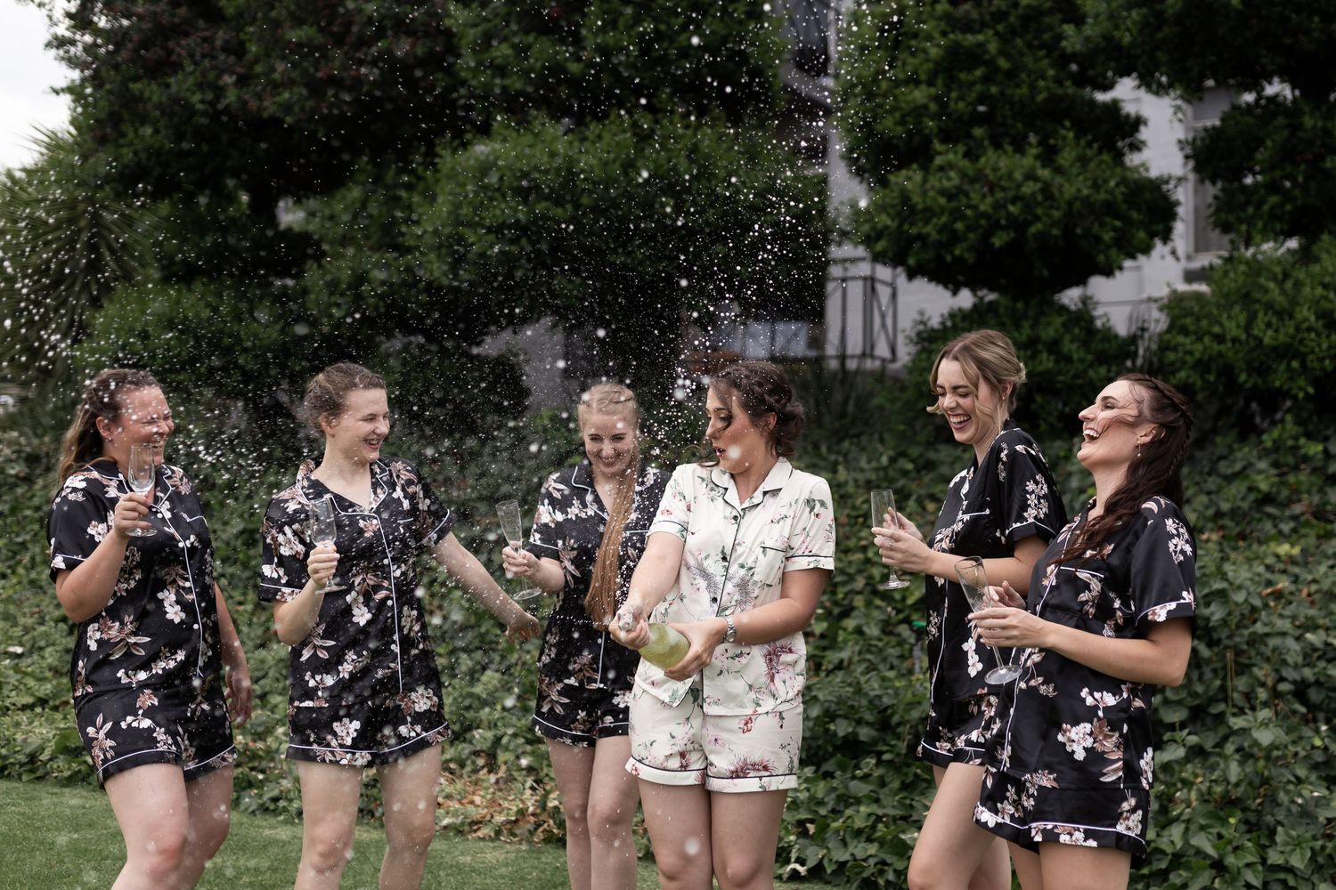 Friends celebrating outdoors with champagne spray and laughter.
