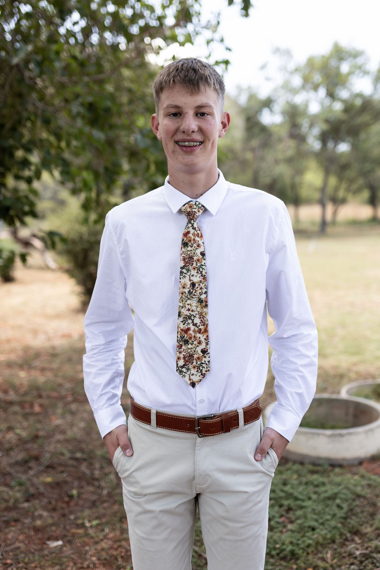 Groomsman in classic white shirt and floral tie smiles for formal portrait.