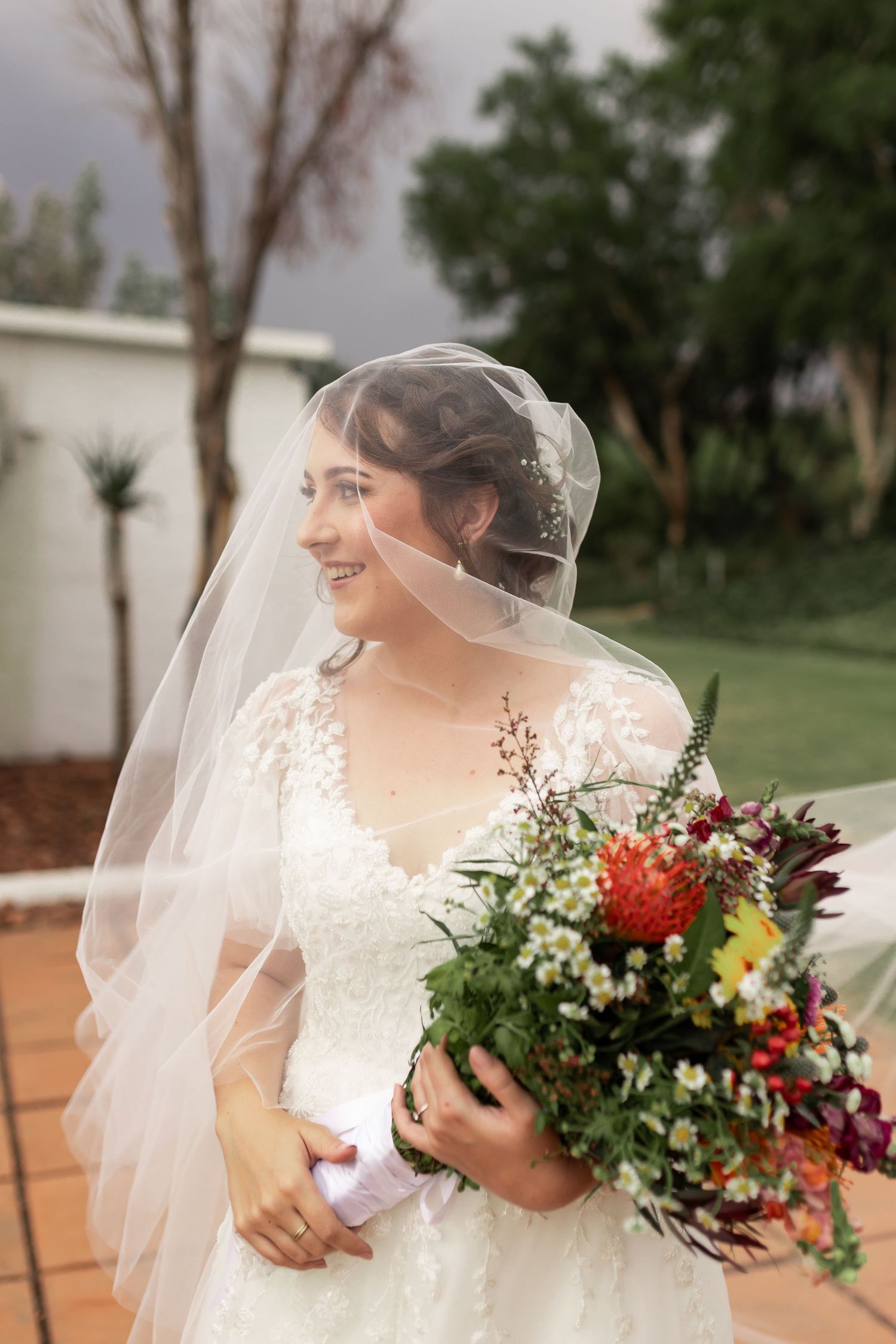 Side profile wedding portrait showcasing a vibrant bouquet of mixed flowers and traditional veil.