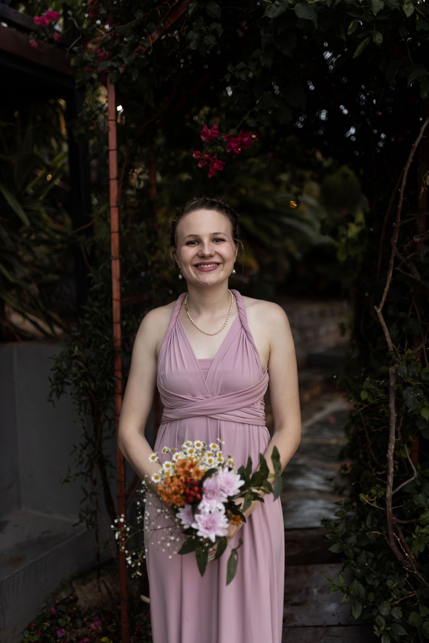 Bridesmaid in dusty rose halter dress holds colorful bouquet in garden setting.