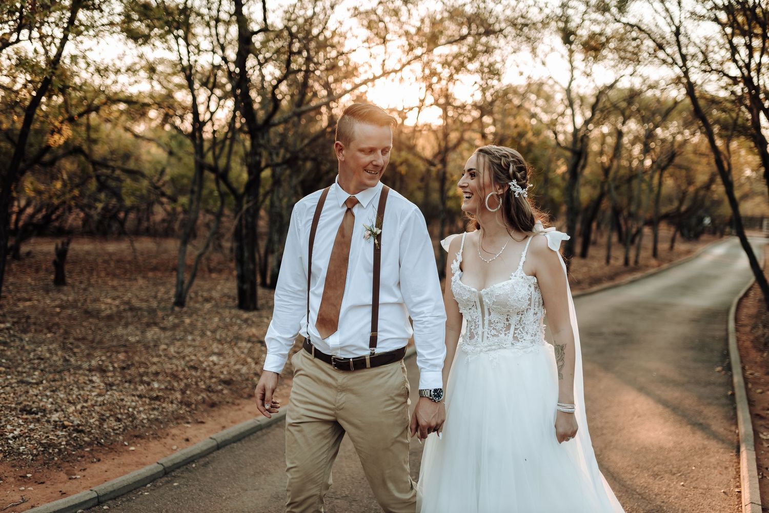 A couple in wedding attire strolling along a winding path through autumn trees.