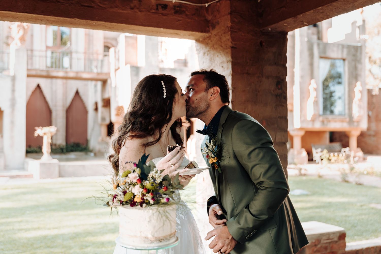A romantic outdoor wedding moment with the couple sharing a kiss under a rustic covered archway.
