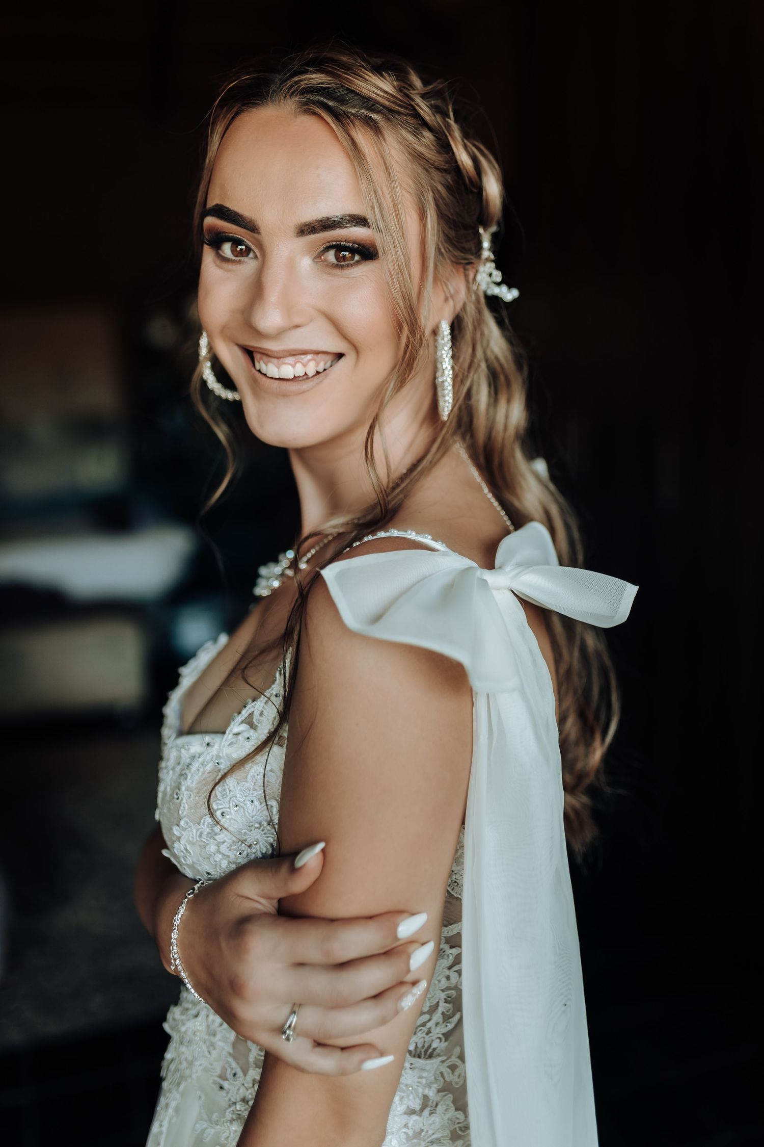 Bride wearing elegant lace dress with bow detail smiles in romantic portrait.