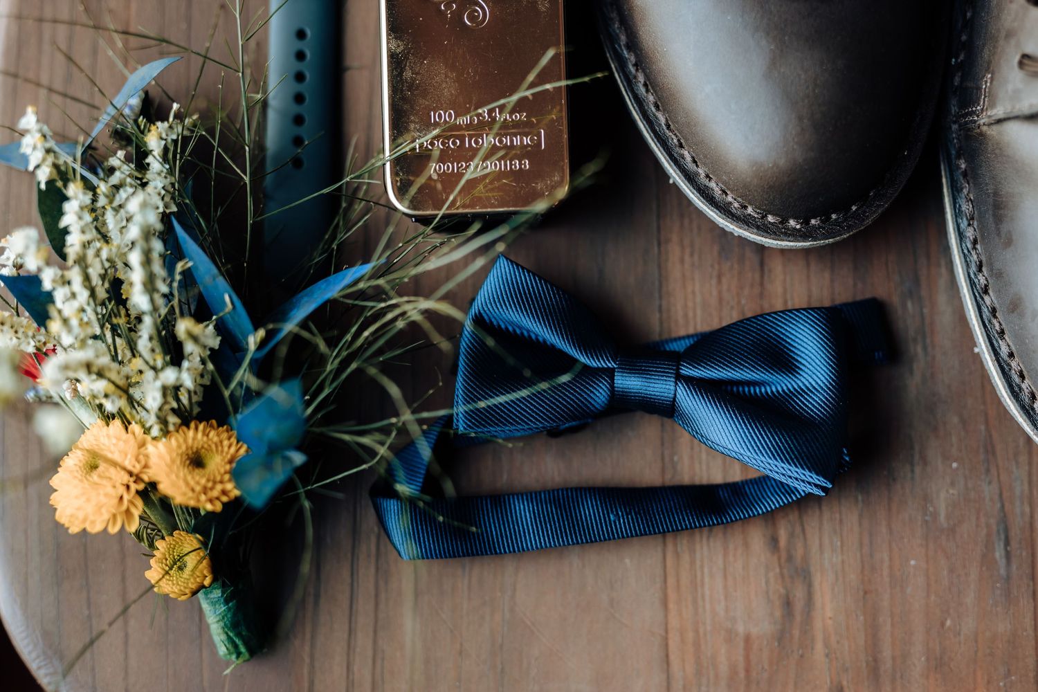 Wedding details with navy blue bowtie, yellow flower boutonniere, and leather shoes.