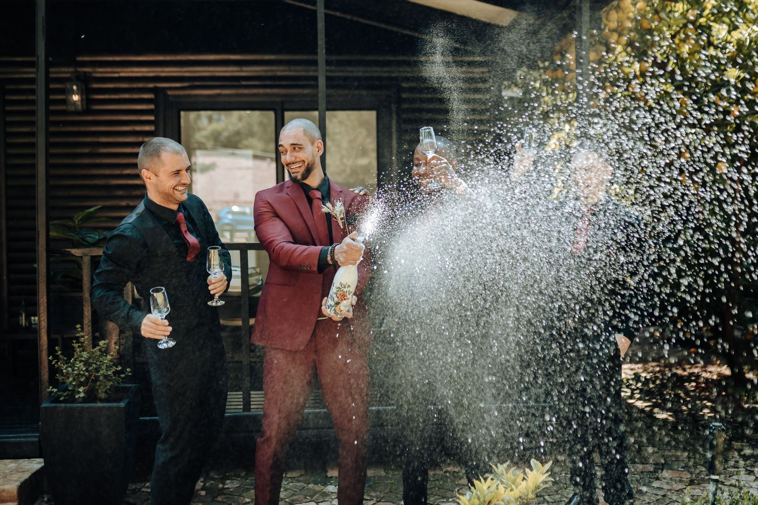 Group celebrating with champagne spray outside a modern building.