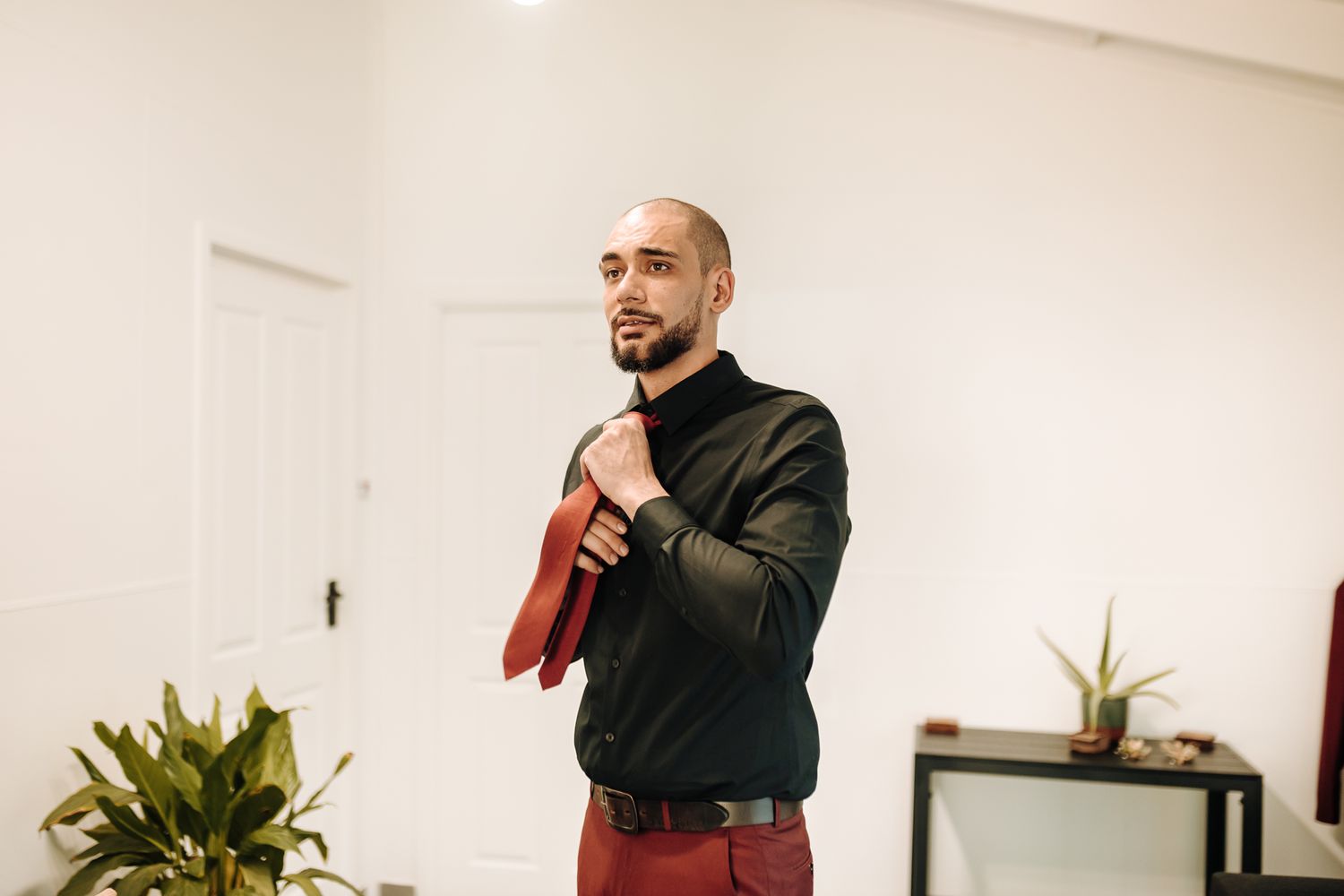 Person adjusting tie while wearing dark shirt in minimalist white room.