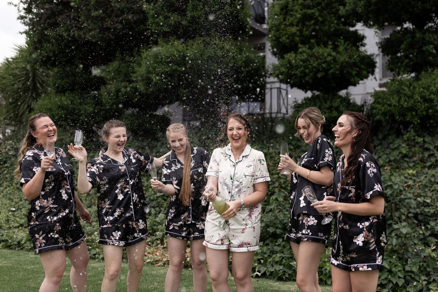 Group enjoying champagne celebration with sprays in garden setting.