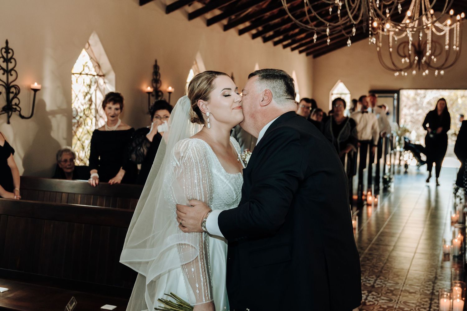 Intimate wedding moment captured inside charming chapel with wooden beams and arched windows.